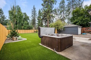 Un patio trasero con un jacuzzi, un cerco de madera, un árbol pequeño y un cobertizo.