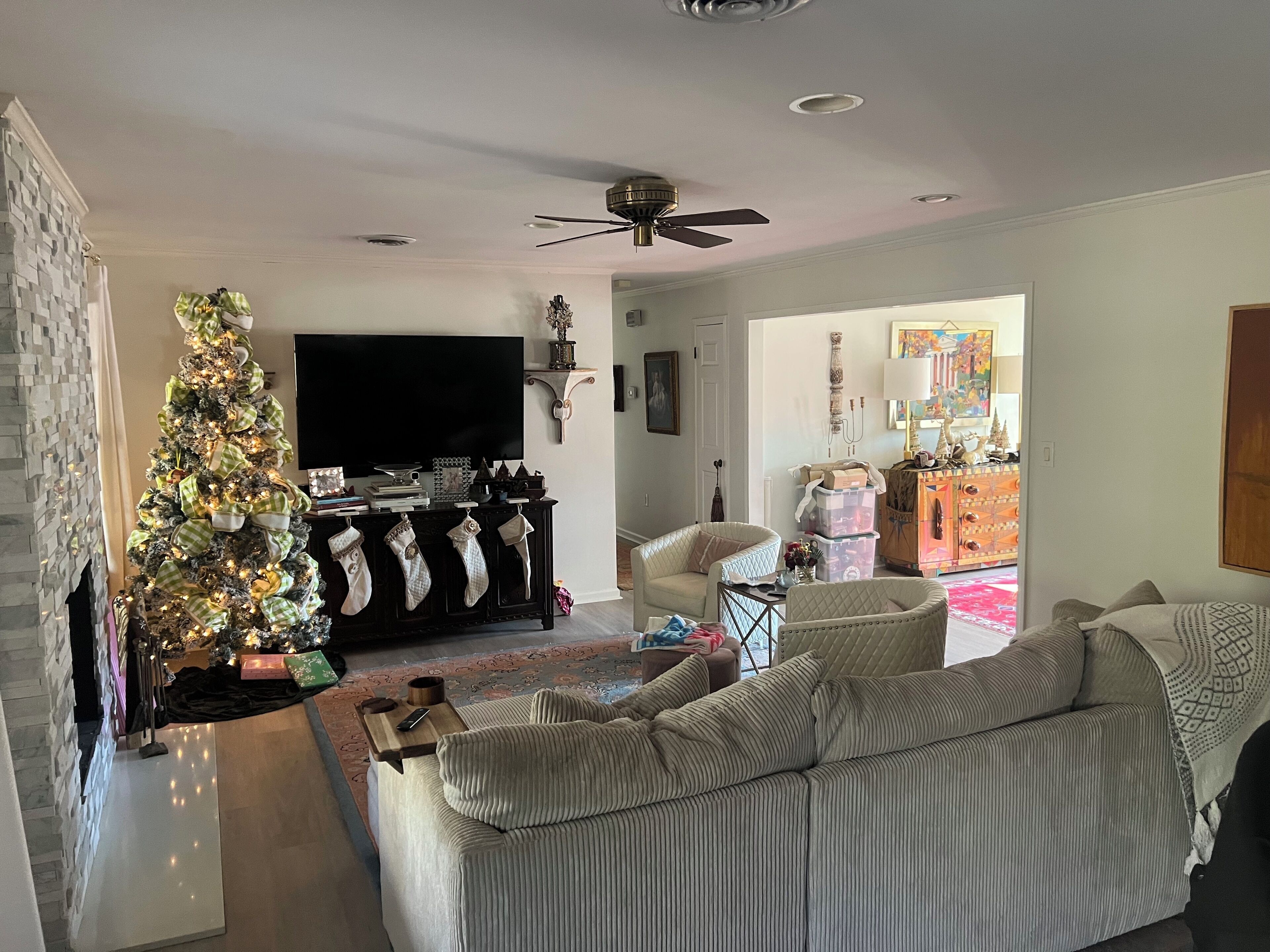 Een woonkamer met een grote flatscreen televisie, een kerstboom, een bank en een plafondventilator.
