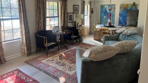 A spacious living room with a large window, a dining area, and a blue sofa with decorative pillows. - Walk to the Grove!From this 3BR 2 Bath!! (Oxford)