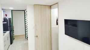 Corredor com porta de madeira, geladeira preta e televisão na parede.