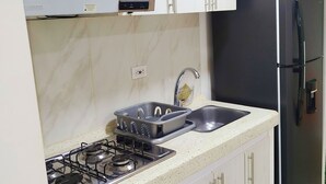 Une cuisine avec des meubles blancs, une cuisinière à gaz, un évier et un réfrigérateur noir.