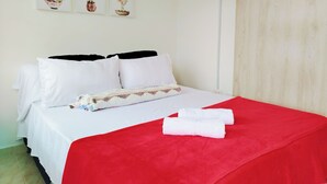 Uma cama bem arrumada com roupa de cama branca e vermelha, um travesseiro com padrão geométrico e uma obra de arte emoldurada acima da cama.