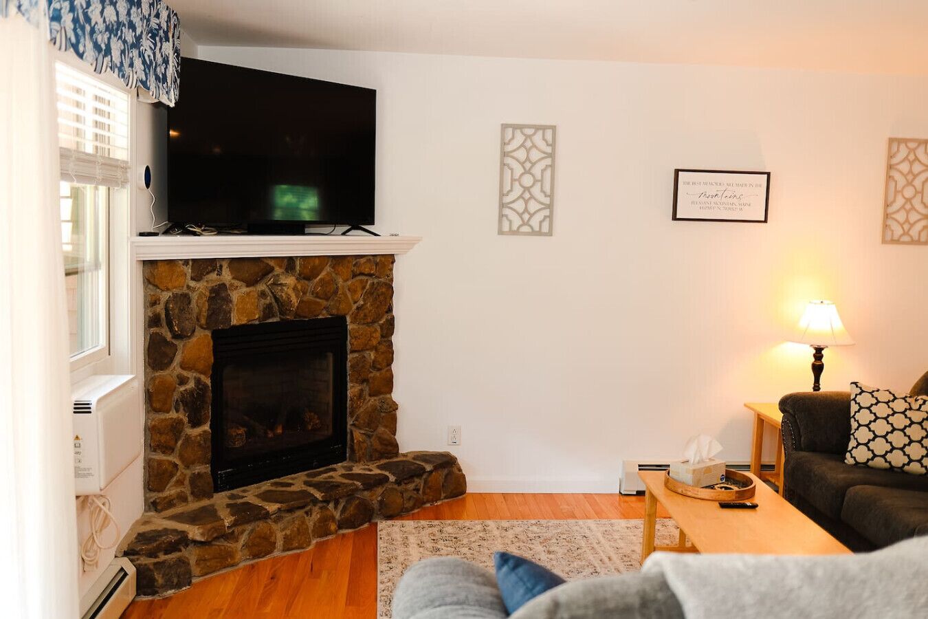 A living room with a stone fireplace, a flat-screen TV mounted above it, a sofa, a coffee table, and a lamp.