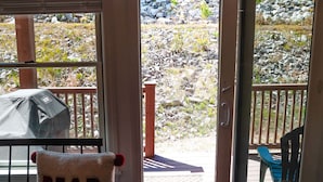 Vista desde adentro de una habitación con una puerta que da a un espacio exterior con un patio, una parrilla y una silla con una toalla que dice 'BEAR HUG'.