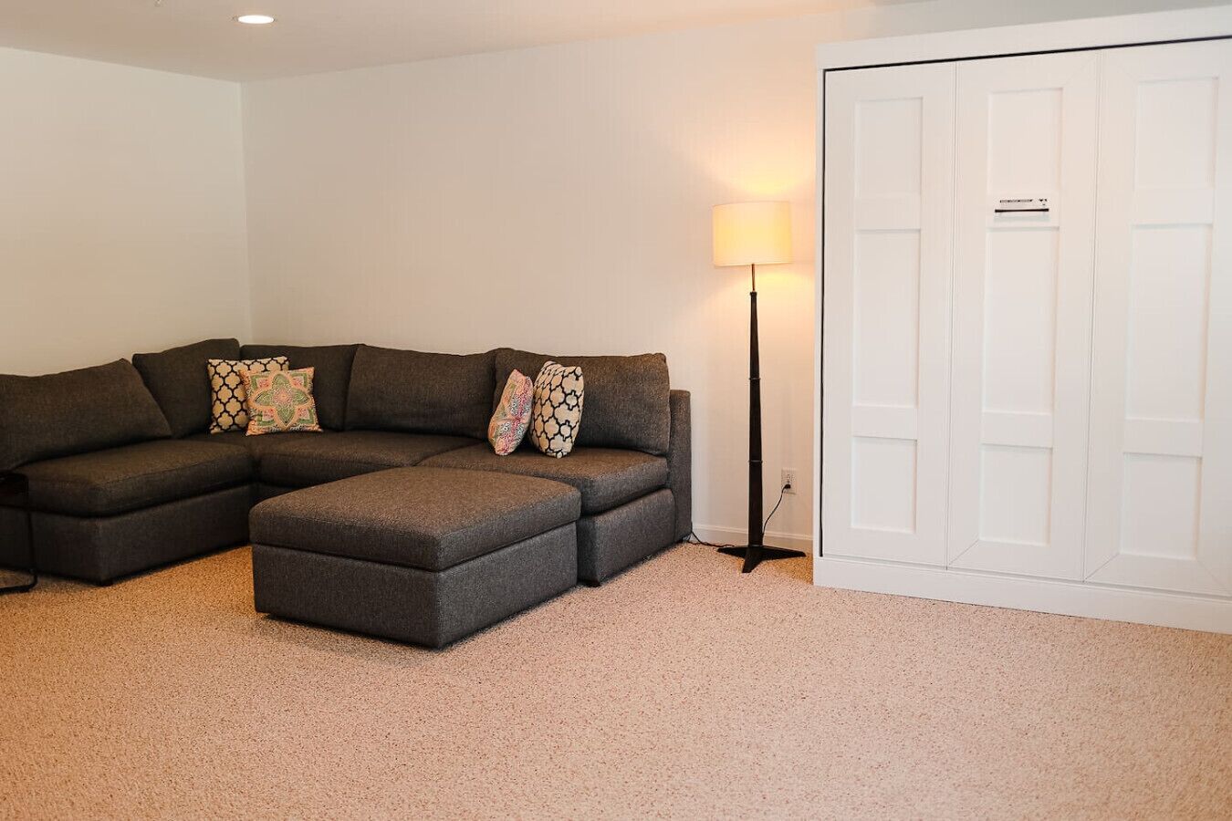 A living room with a sectional sofa, ottoman, and a floor lamp.