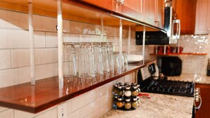 Una cocina con encimera de madera, repisa de vidrio con varios vasos, y una estufa.