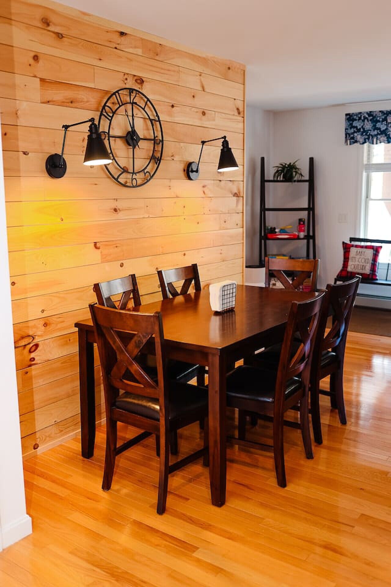 Un comedor con pared de madera, un reloj y dos lámparas de pared.
