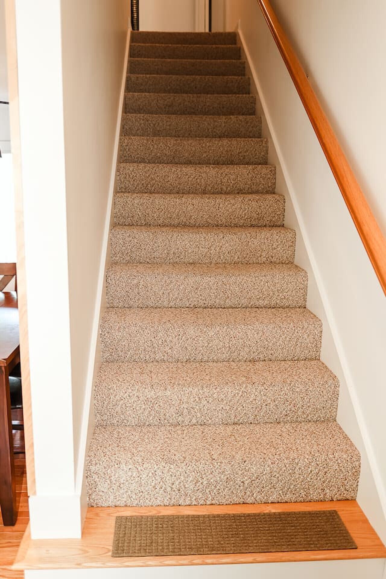 Una escalera alfombrada con barandillas de madera y un felpudo al pie.