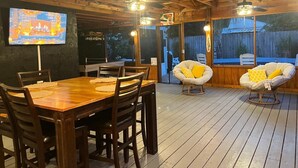A wooden deck with a dining table and chairs, a TV mounted on the wall, and two ceiling fans. - Wonderful 3-bedroom house in St. Augustine, close to beach and Historic District (St. Augustine)