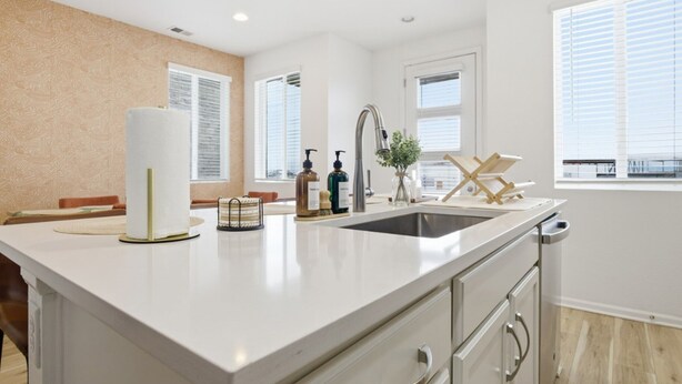 Een moderne keuken met een groot eiland, witte kasten en een raam met zonwering.