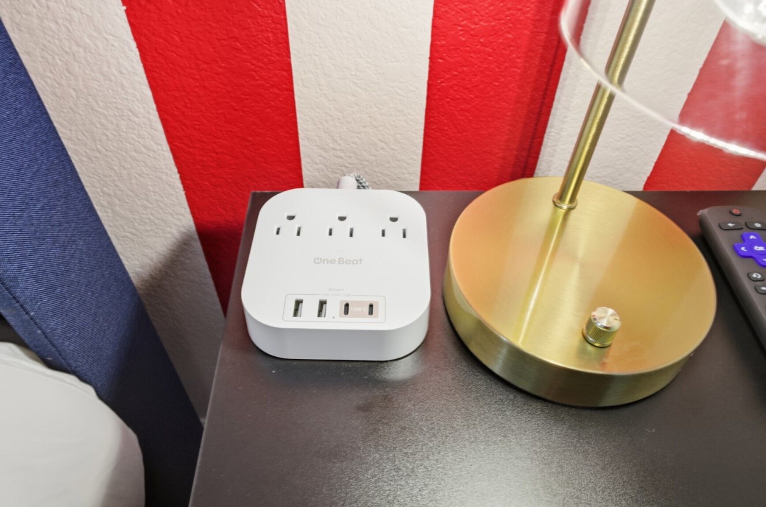 A OneBeat power strip on a table with a lamp and a remote control.