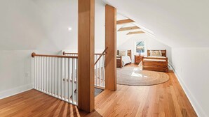 Ruime zolderkamer met houten balken, een houten trap, een rond tapijt en een bed met nachtkastje.