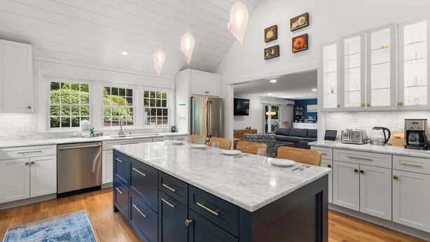 A modern kitchen with a large island, white cabinetry, and a dining area with a sofa and coffee machine.