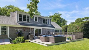 A two-story house with a patio, outdoor seating, and a fenced backyard.