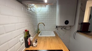 A kitchen with white tiled walls, a wooden countertop, a black induction cooktop, a stainless steel sink, and a water heater. - Arroios Elegance Residence - Lisbon Center (Lisboa)