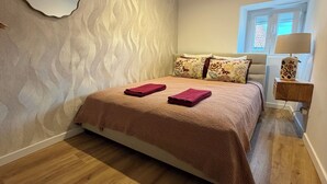 A bedroom with a bed, wooden flooring, a wall mirror, and a window with blinds. - Arroios Elegance Residence - Lisbon Center (Lisboa)
