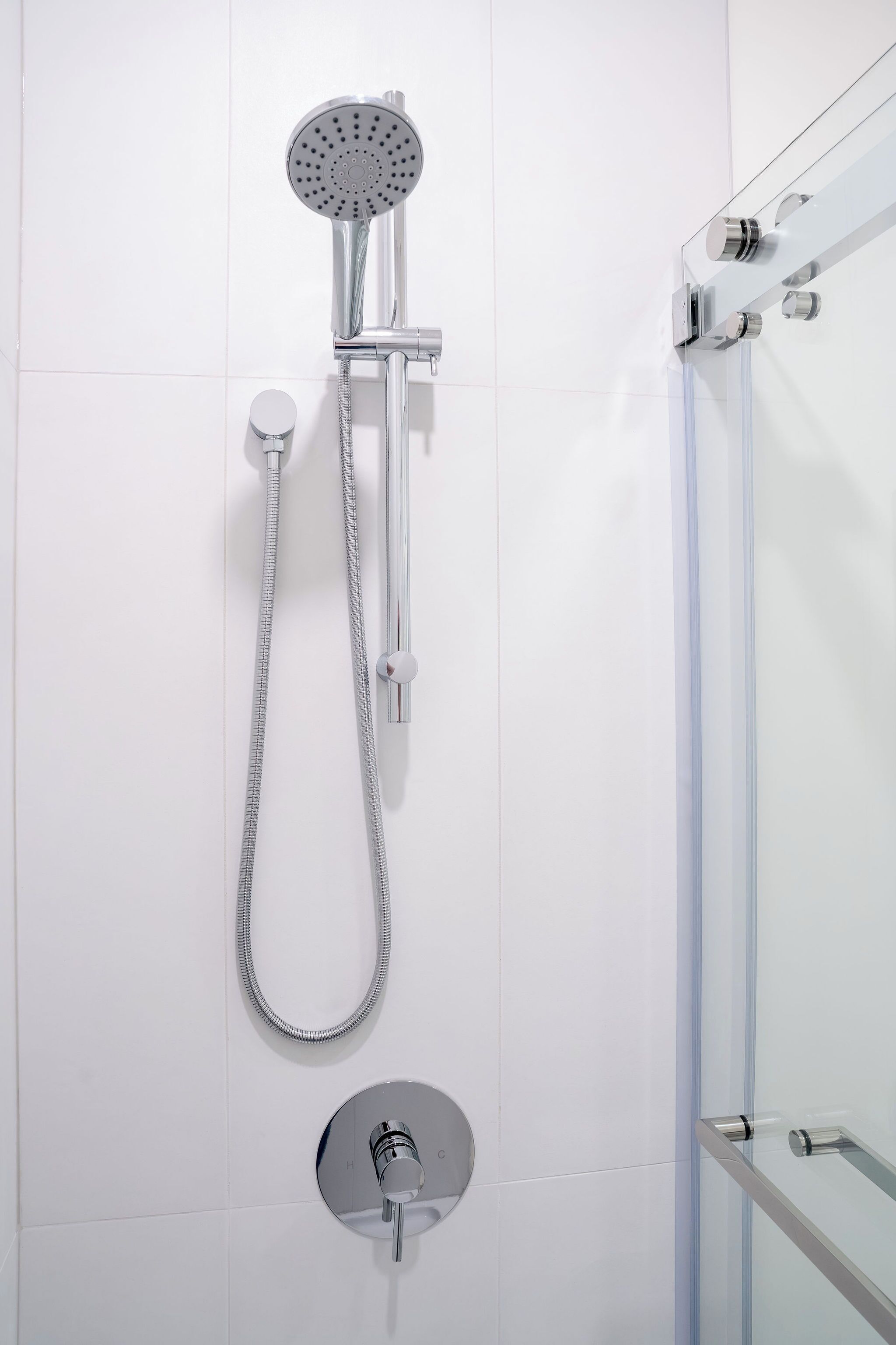 A modern shower with a handheld showerhead and a fixed wall-mounted showerhead, both with chrome finishes.