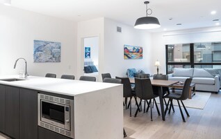 Una cocina moderna con horno empotrado, un comedor con mesa y sillas de madera, y una sala de estar con sofá y mesa de centro.