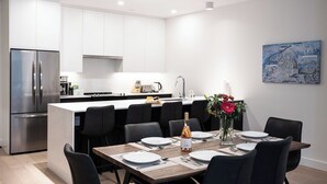 A modern kitchen with white cabinets, a stainless steel refrigerator, and a dining area with a wooden table set for four. - Bluebird by Revelstoke Vacations (Revelstoke)