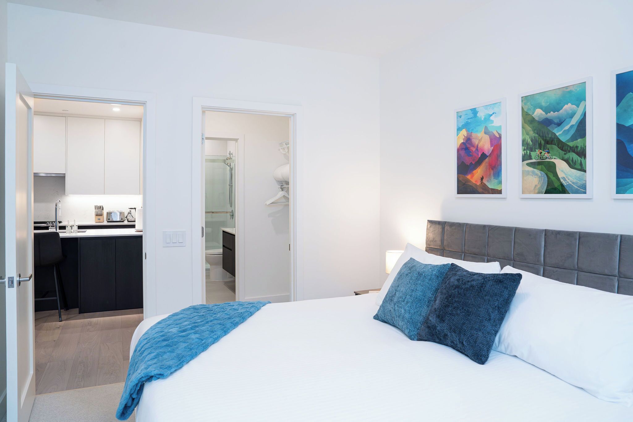 Une chambre d’hôtel moderne dotée d’un grand lit, d’une kitchenette séparée et d’une salle de bain visible à travers une porte ouverte.