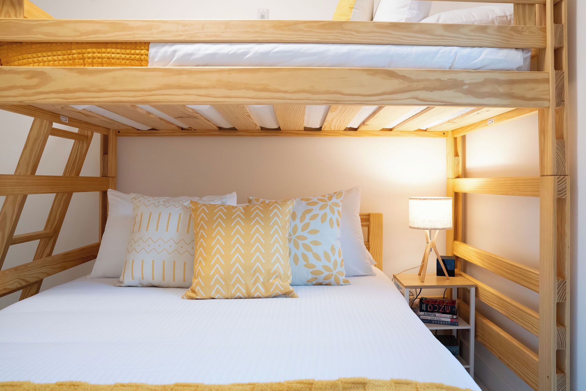 Un lit superposé avec une tête de lit en bois, une table de chevet avec une lampe et des coussins à motifs.