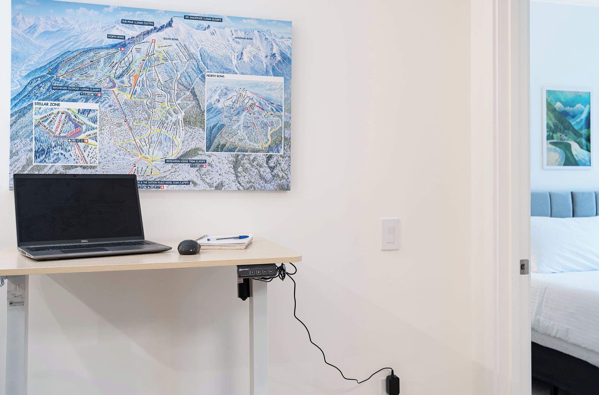 A hotel room with a desk featuring a laptop, a mouse, and a map.