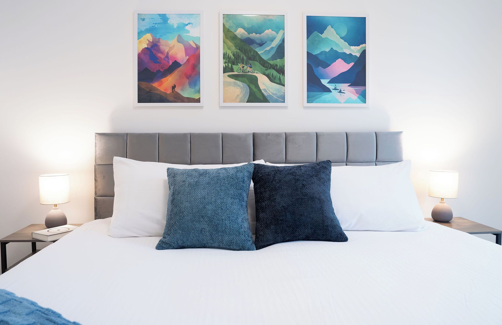 Een hotelkamer met een groot bed, twee bedlampjes en drie kunstwerken boven het bed.