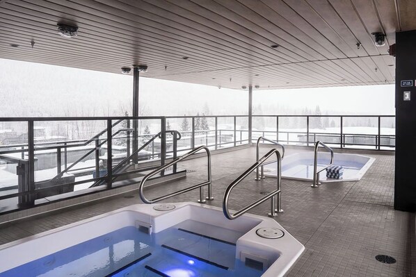 A spa area with two hot tubs and a view of a snowy landscape. - Bluebird by Revelstoke Vacations (Revelstoke)
