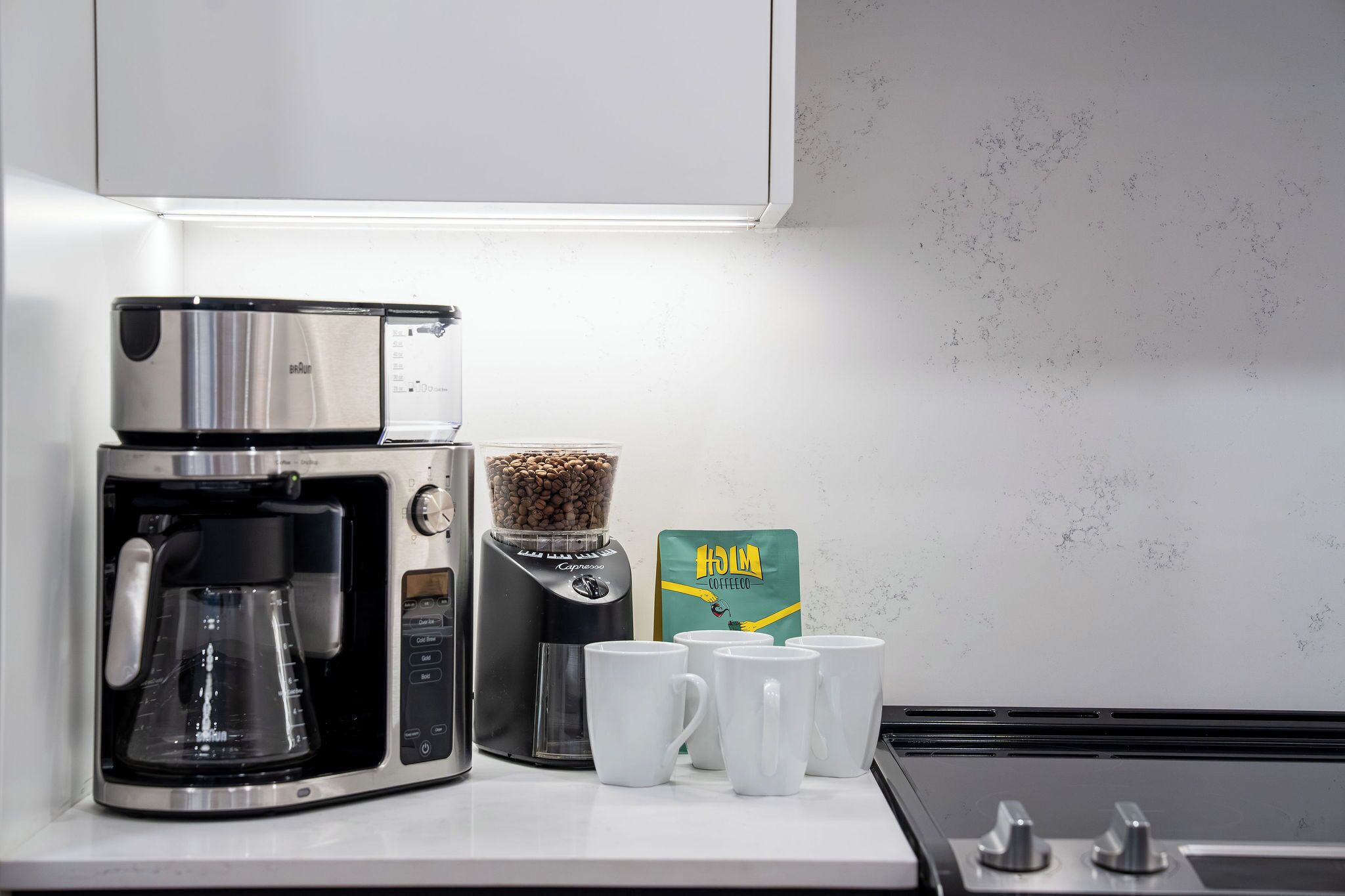 Una cafetera, un molinillo de café y un paquete de granos de café sobre una encimera de cocina.