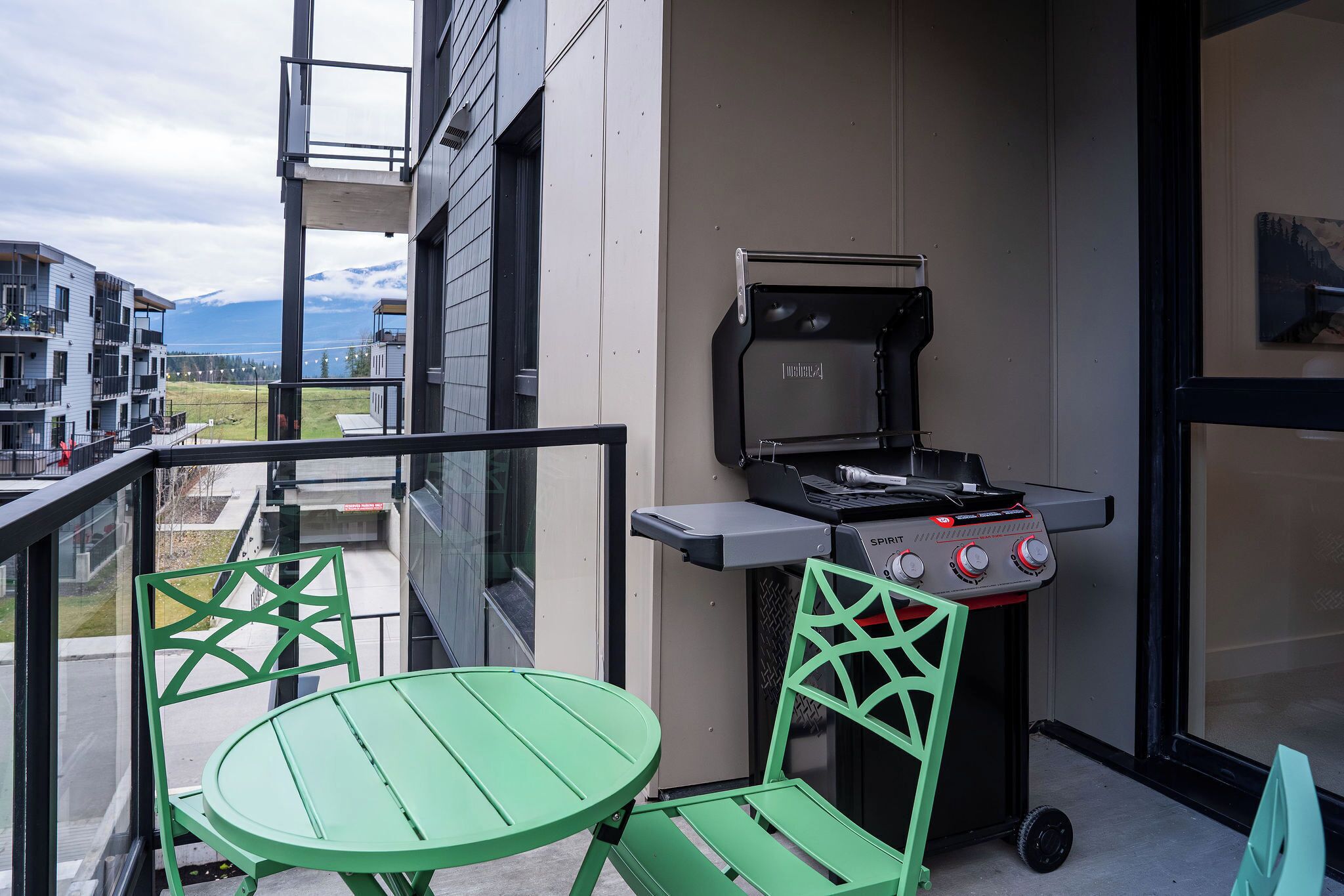 A balcony with a grill, green chairs, and a table.