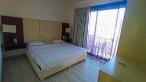 Une chambre d’hôtel avec un grand lit, une table de chevet, une commode et une fenêtre avec des rideaux.