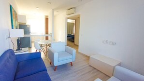 Un salon moderne avec un canapé bleu, un fauteuil blanc et un divan blanc. On aperçoit à l’arrière-plan un coin repas avec une table et des chaises.