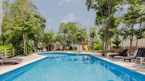 A clear blue swimming pool surrounded by lounge chairs and trees, with a slide in the background. - Beautiful, cozy & comfortable house Puerto Morelos (Puerto Morelos)