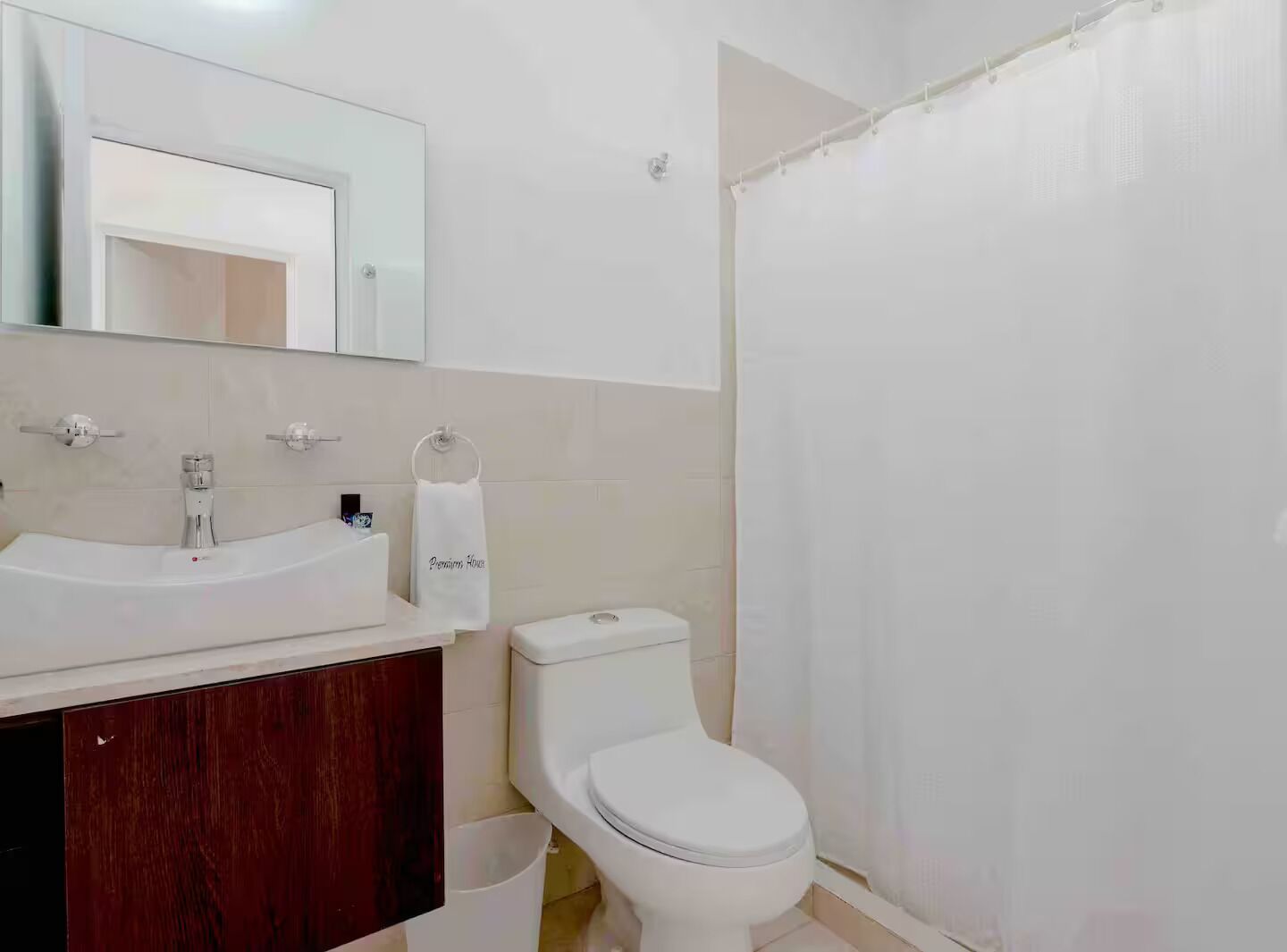 Baño con lavamanos blanco, espejo encima, inodoro y cortina de ducha.