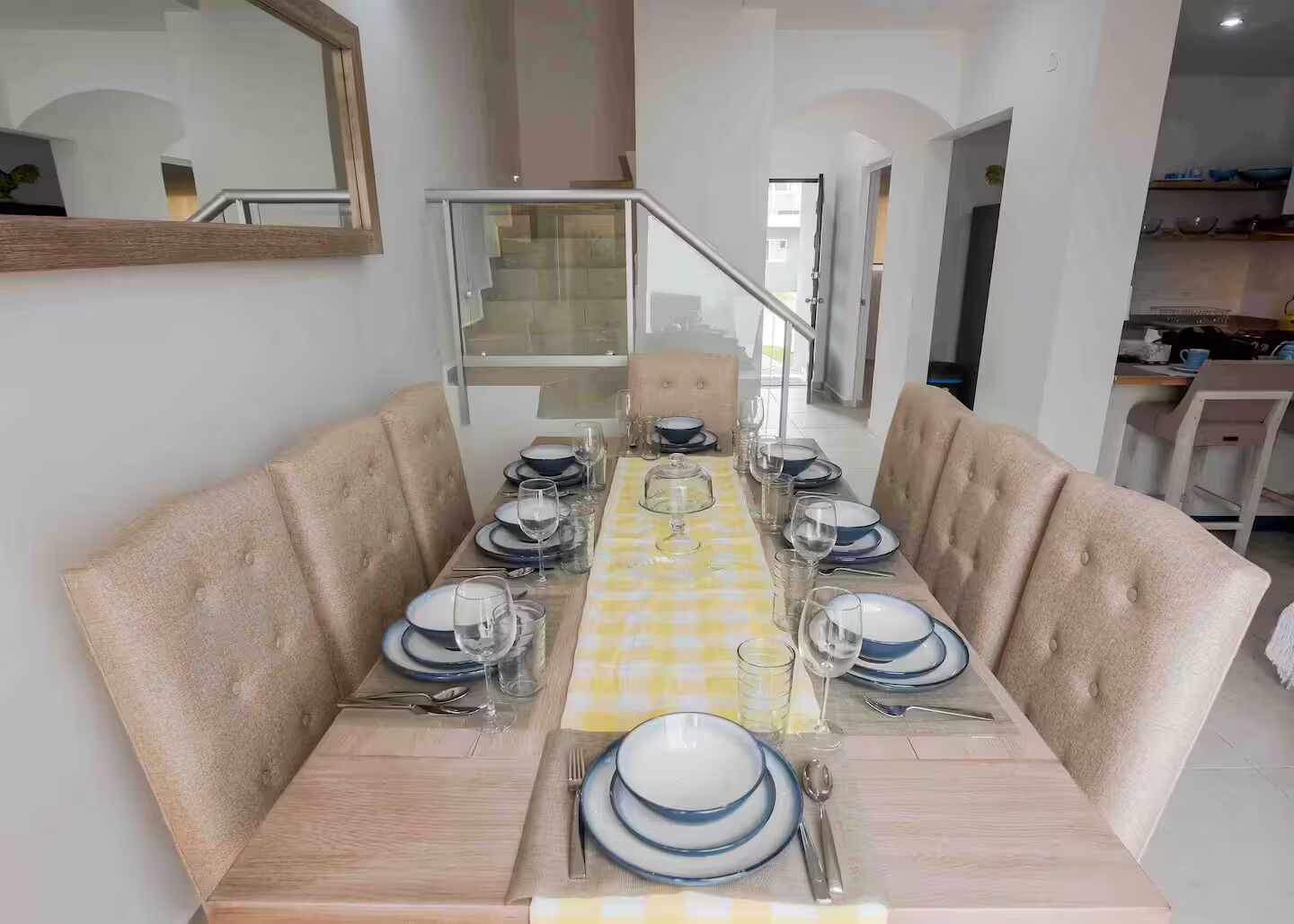 Un comedor con una mesa larga dispuesta para seis personas, sillas tapizadas y un mantel a cuadros.