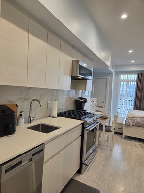 A modern kitchen with a dishwasher, stove, and sink. There is a dining area with a table and chairs. - Furnished studio, all incl, pet-friendly, view, Landmark District, Kelowna. (Kelowna)