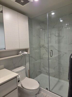 A modern bathroom with a glass shower enclosure, a toilet, and a vanity with a mirror. - Furnished studio, all incl, pet-friendly, view, Landmark District, Kelowna. (Kelowna)