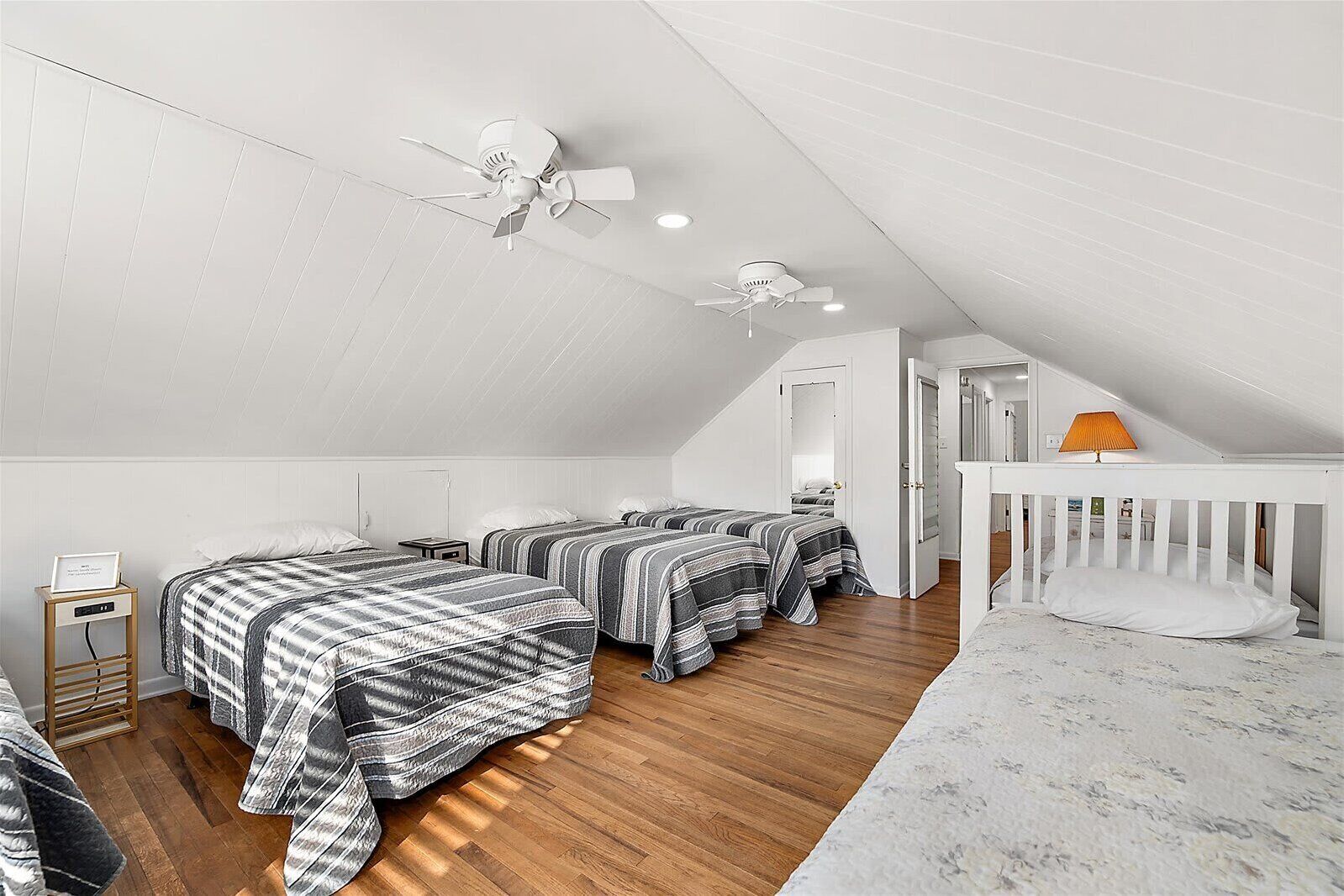 A bedroom with two beds, a crib, a ceiling fan, and a wooden floor.