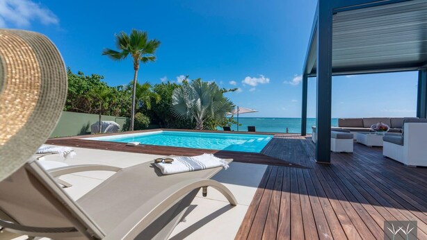 A modern outdoor pool area with a wooden deck, lounge chairs, and a view of the ocean. - Montepulciano (Saint François)