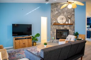 Ein Wohnzimmer mit Flachbildfernseher, Kamin aus Naturstein und Deckenventilator.
