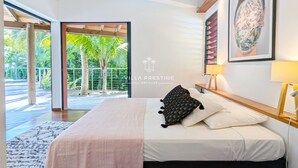 A modern bedroom with a bed, a large window, and a view of palm trees. - Coco Verde (Petit-Bourg)