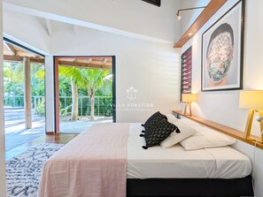 Ein modernes Schlafzimmer mit Bett, großem Fenster und Blick auf Palmen.