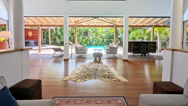 A spacious indoor area with a wooden floor, a large rug, and a pool visible through an open structure. - Coco Verde (Petit-Bourg)