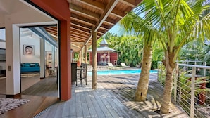 A wooden deck with a pool, palm trees, and a covered seating area. - Coco Verde (Petit-Bourg)