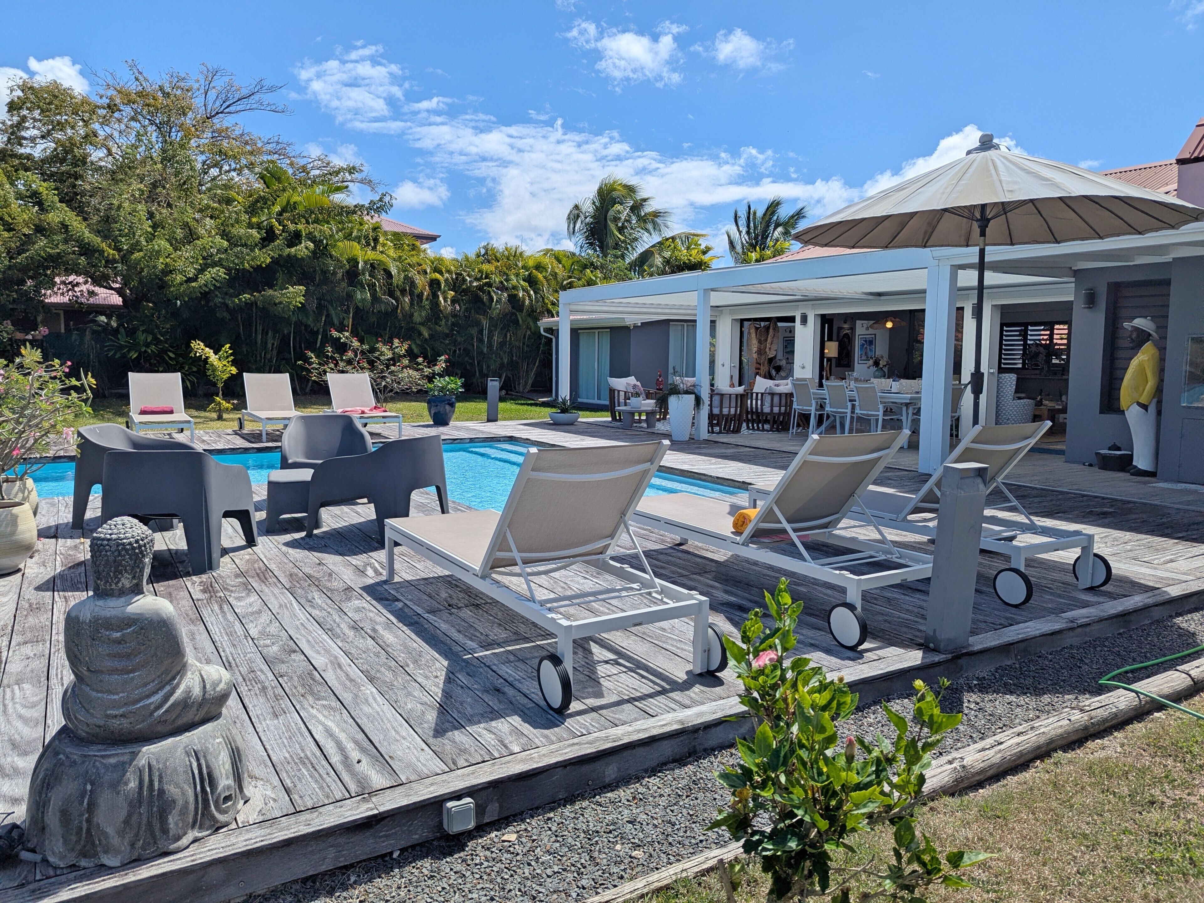 A poolside area with lounge chairs, a statue, and a covered patio with tables and chairs.
