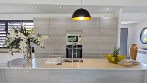 A modern kitchen with a central island, stainless steel appliances, and a black pendant light. - Rubis |Exclusivité (Saint François)