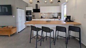 Een moderne keuken met een centraal eiland, zwarte barkrukken en hanglampen.