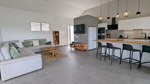 Een moderne woonkamer met een bank, salontafel en een keukenhoek met barstoelen.