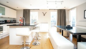 Una cocina moderna con armarios blancos, una isla central con taburetes, una mesa de comedor y vistas al exterior.