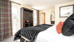 Habitación de hotel con cama, cabecera negra, almohada roja, almohada negra, pared blanca, cuadro enmarcado y ventana con cortinas.